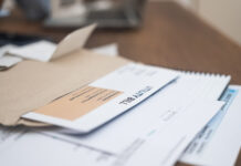 Utility bill statement details, displaying due amount, alongside a phone calculator, set on a wooden apartment table. Financial responsibility in focus.